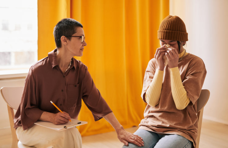 short haired female psychologist comforting young woman crying